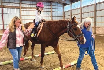 MacKenna Pence riding Rocky at Untamed Spirit. Her mom, Ruth, and owner Barbara Ford guide her during a ride.